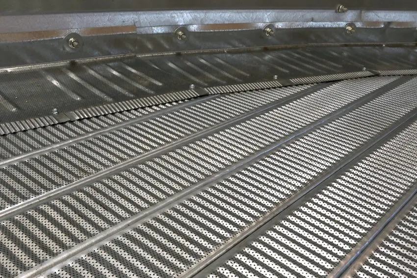 A curved, metallic structure with vertical slatted dividers arranged on a concrete floor, likely a livestock confinement pen